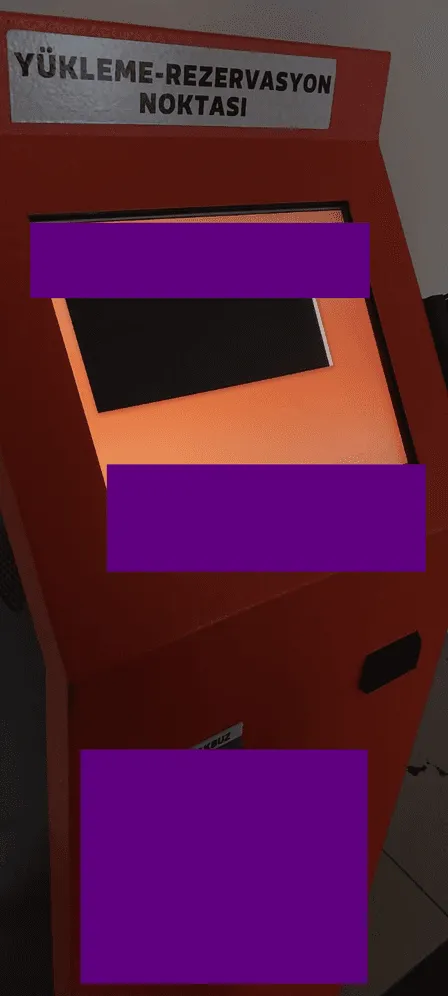Photo of an orange self-service kiosk labeled Yukleme-Rezervasyon Noktasi, parts of it redacted by purple boxes.